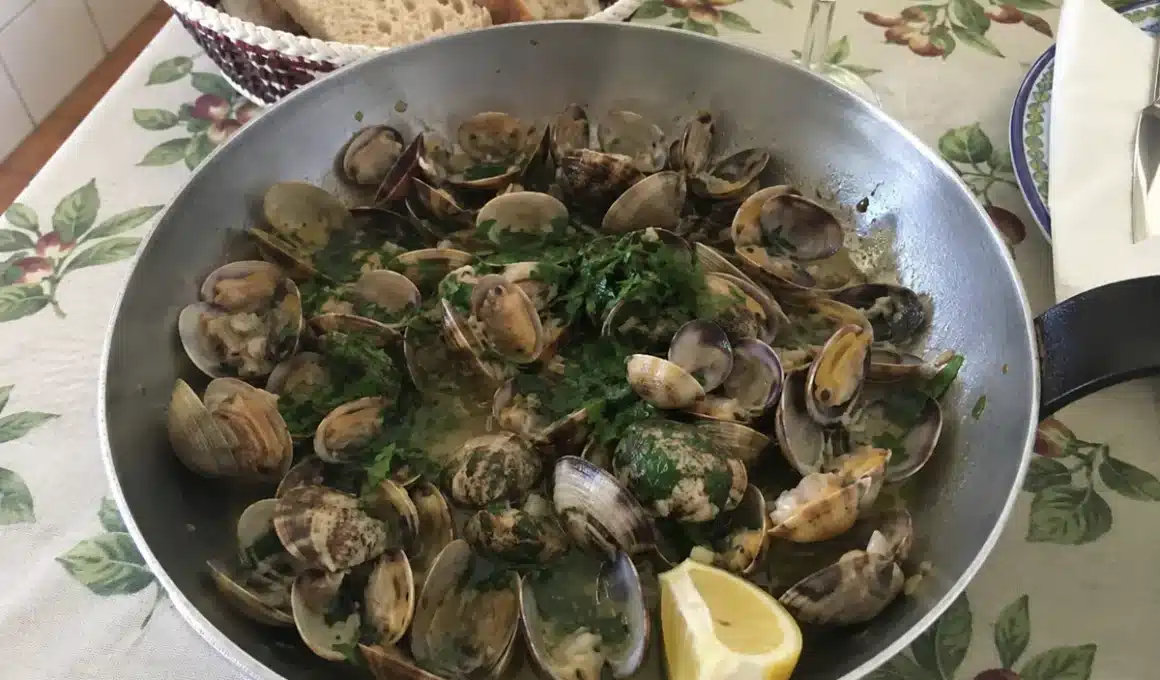 Poêle d'ameijoas à Bulhão Pato fumantes au centre d'une table familiale, avec pain rustique et vin blanc