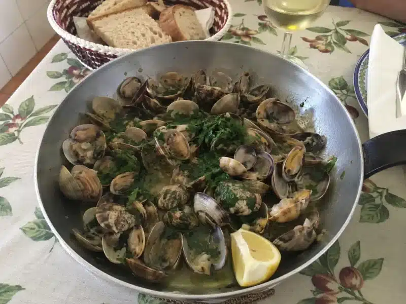 Poêle d'ameijoas à Bulhão Pato fumantes au centre d'une table familiale, avec pain rustique et vin blanc