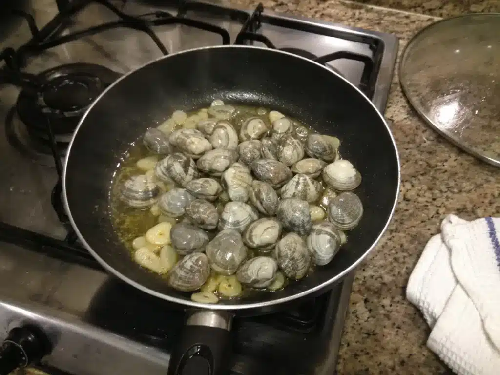 Palourdes crues versées sur l'ail blondi à l'huile d'olive dans une poêle, début de la cuisson flash